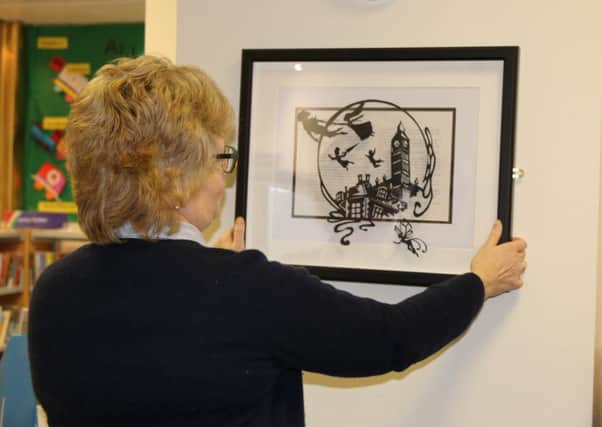 Mairi White, library supervisor at Melrose Library, hangs the anonymously donated Peter Pan picture.